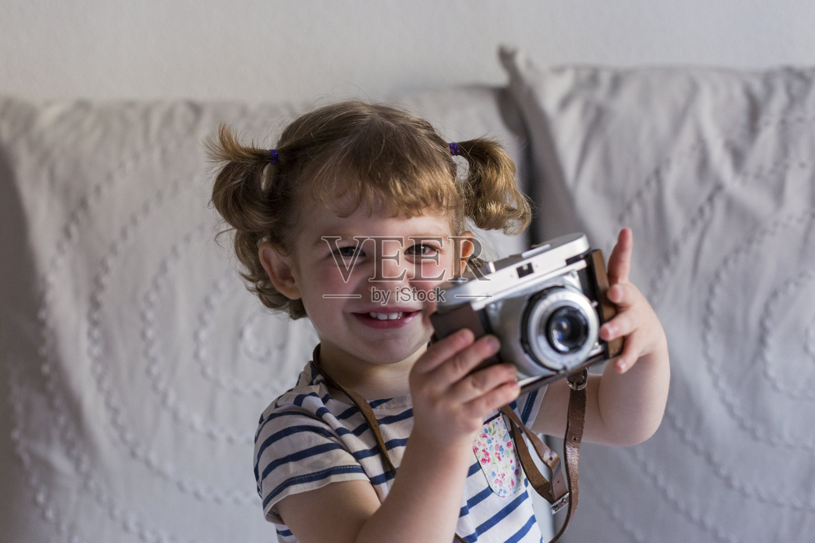 美丽快乐的小女孩坐在床上，用着一台老式相机。家,在室内的概念。生活方式照片摄影图片