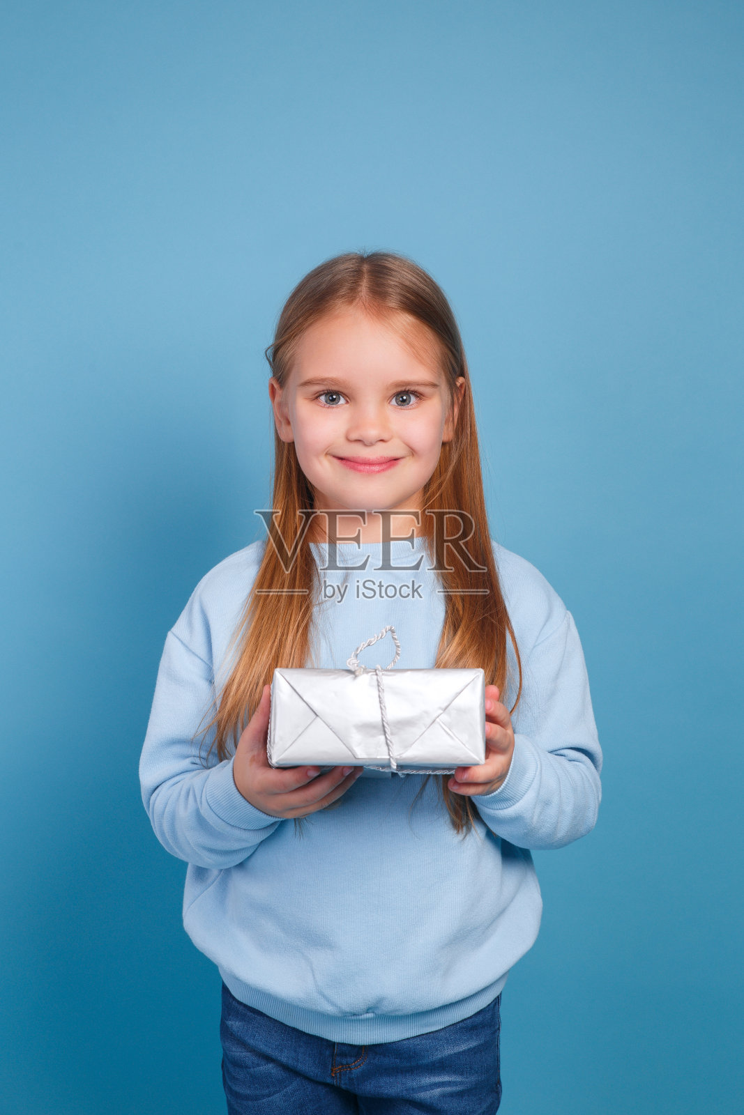 一个小女孩的肖像在一个温暖的针织毛衣与礼品盒在青色的背景照片摄影图片