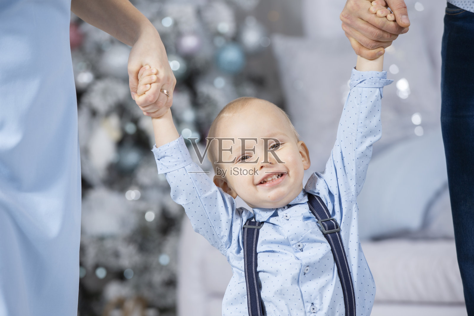 祝宝宝和父母圣诞快乐。妈妈和爸爸的手抱着孩子在圣诞树的背景下。一个小男孩的脸在新年。家人在寒假。照片摄影图片