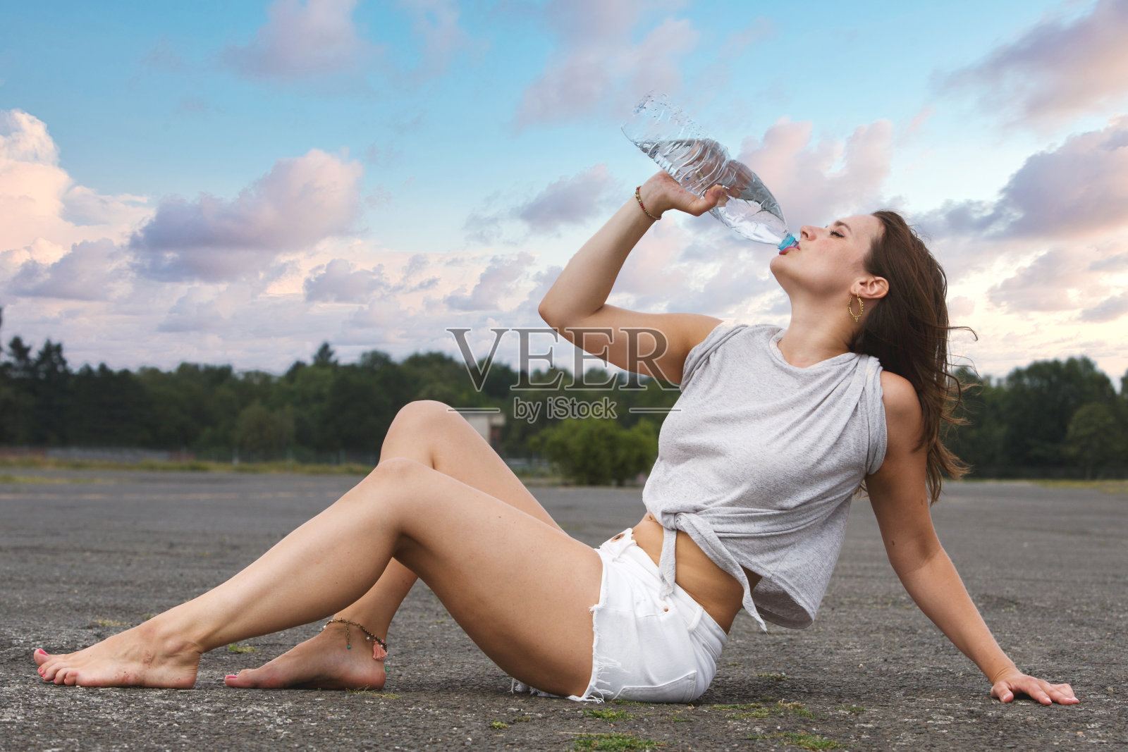 穿着短裤的年轻女子坐在人行道上喝着水照片摄影图片