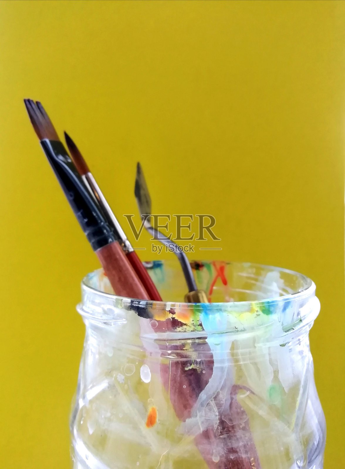 艺术笔刷和调色板刀放在一个玻璃罐子里，在黄色的背景上。照片摄影图片