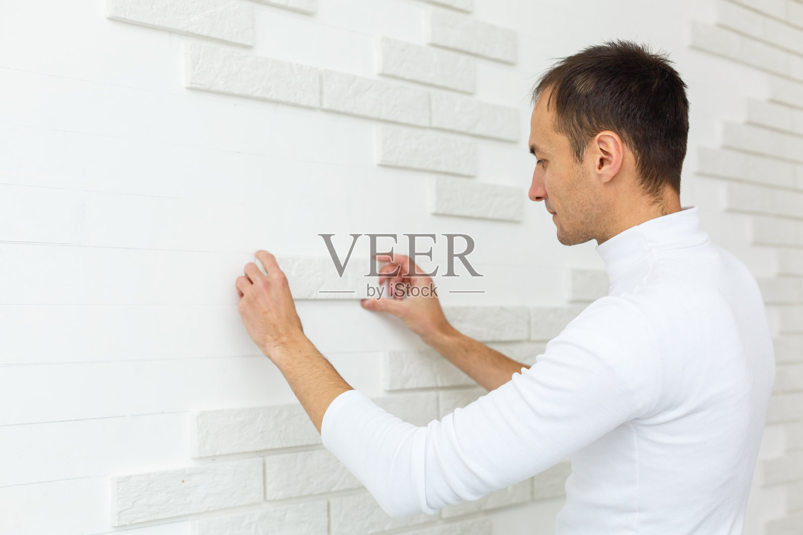 时尚新潮的白色瓷砖与厨房墙上的一个倒角。在浴室墙壁上铺设白色矩形瓷砖的过程中，瓷砖工人的手。公寓和浴室的维修。照片摄影图片