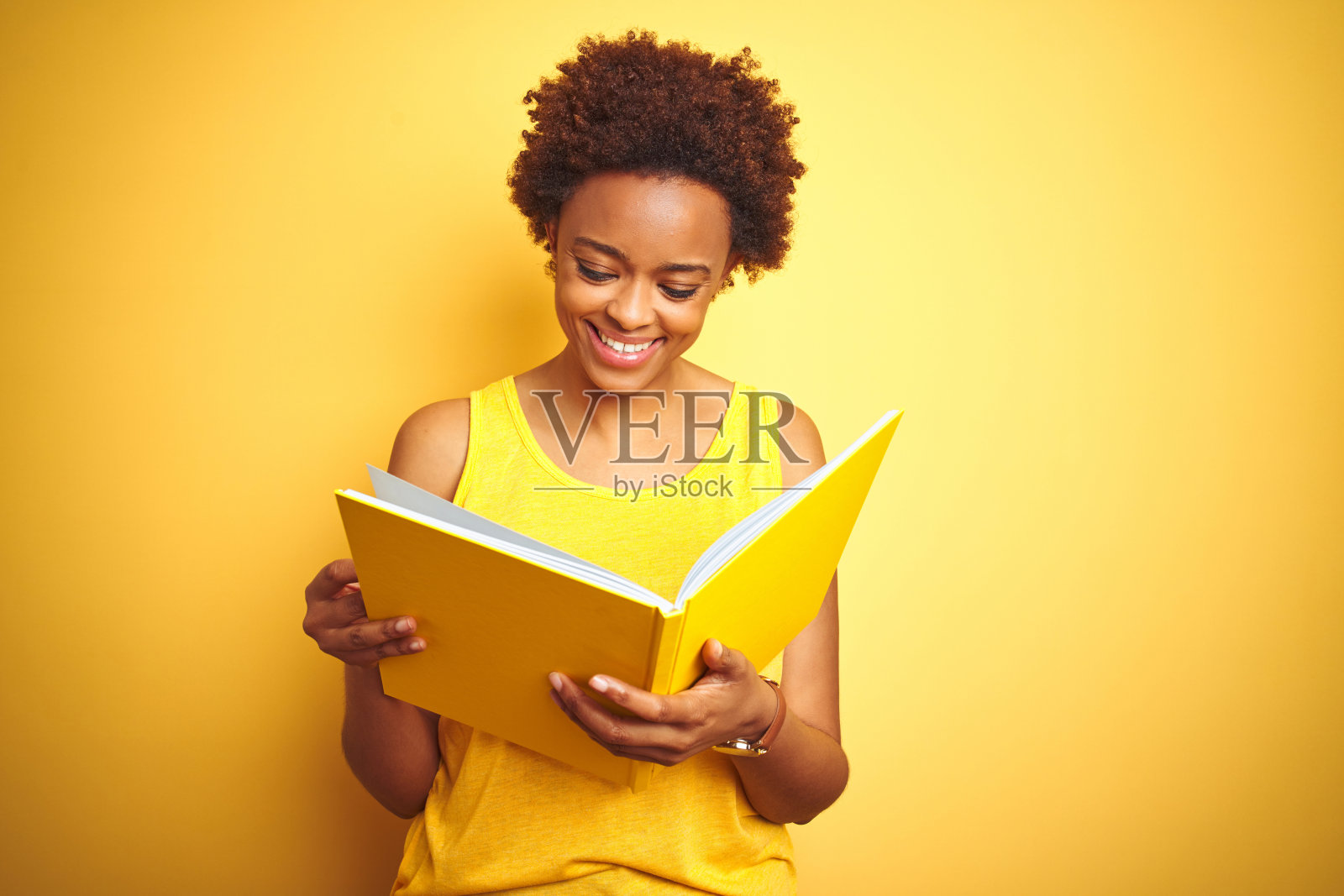 非洲裔美国妇女读一本书在黄色孤立的背景与一个快乐的脸站在微笑与自信的微笑显示牙齿照片摄影图片