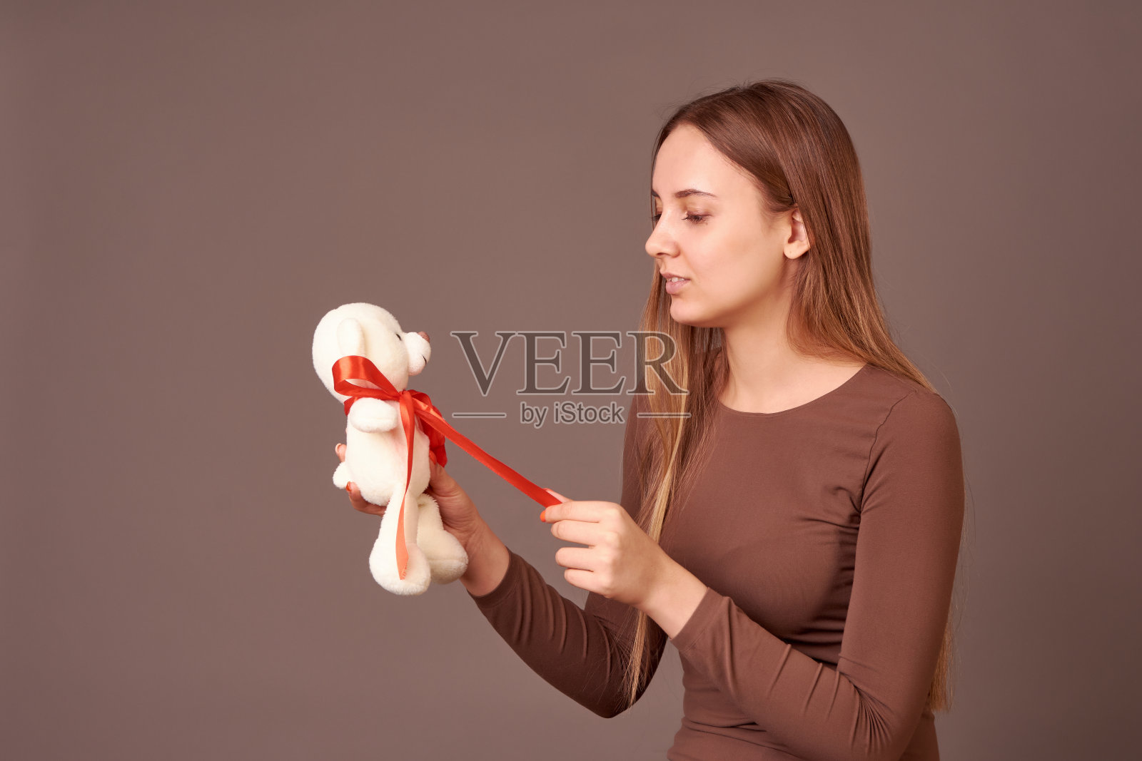 灰色背景上的女孩手里拿着一只玩具熊。生日礼物，情人节礼物。照片摄影图片