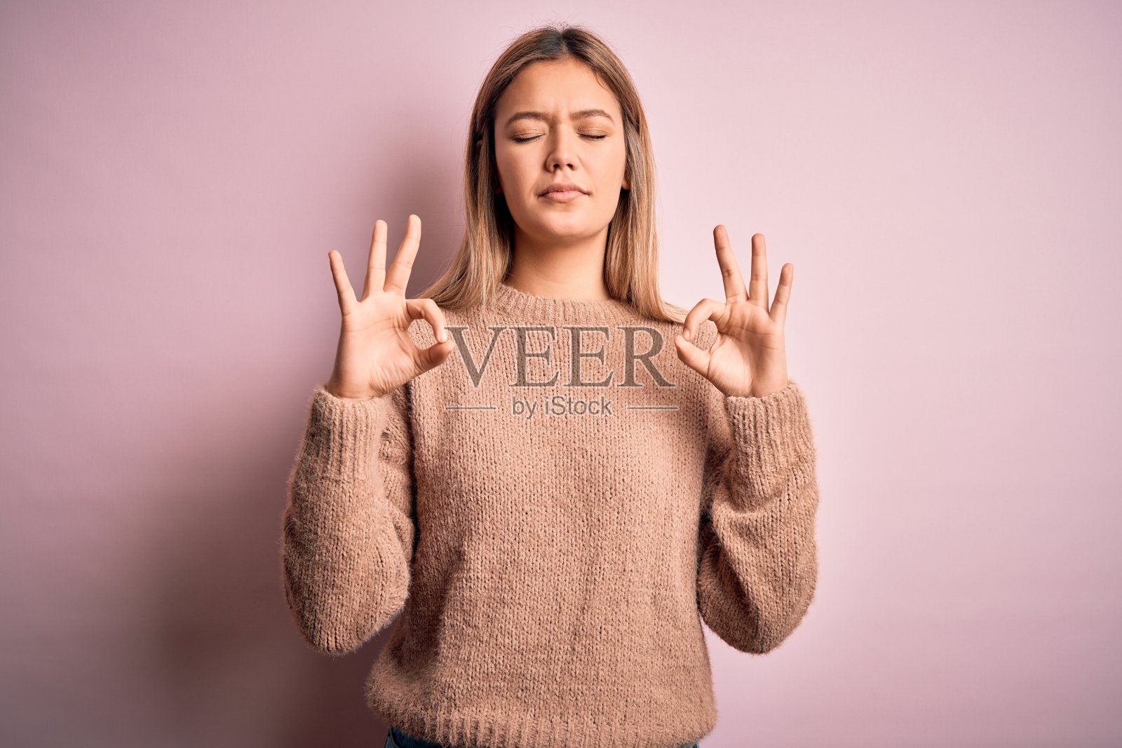 年轻美丽的金发女人穿着冬天的羊毛衫在粉红色孤立的背景放松和微笑闭着眼睛做冥想手势与手指。瑜伽的概念。照片摄影图片