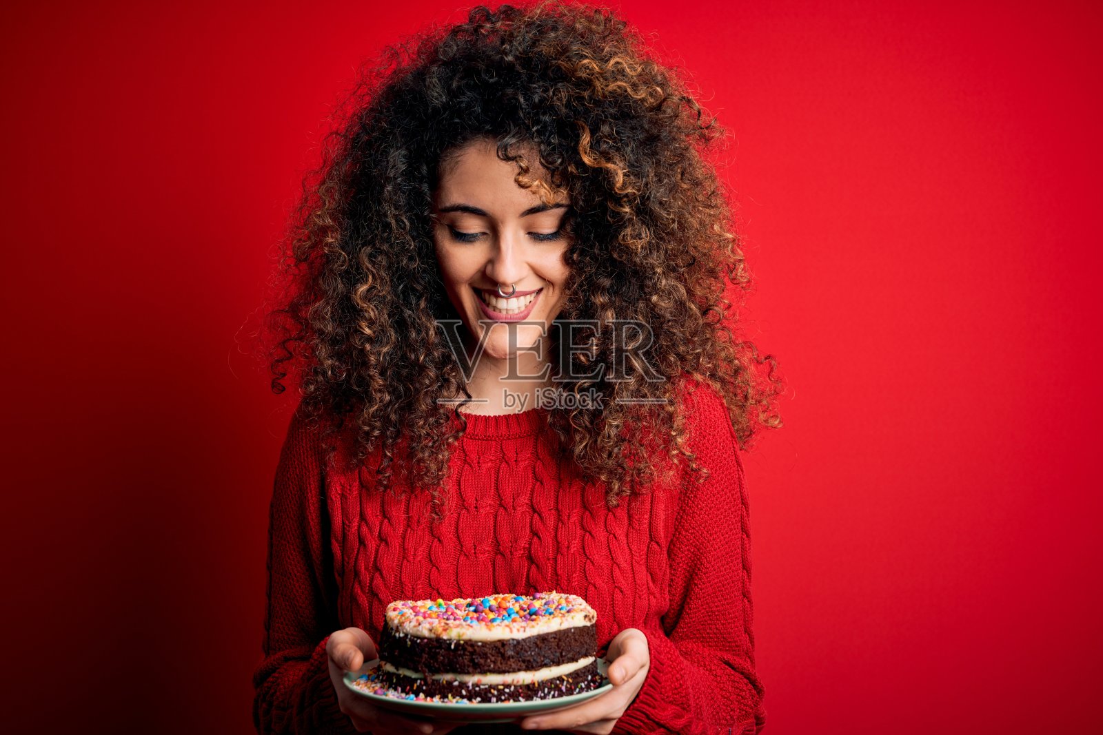 年轻美丽的女人与卷曲的头发和穿洞持有盘子与生日蛋糕与一个快乐的脸站着和微笑与自信的微笑显示牙齿照片摄影图片