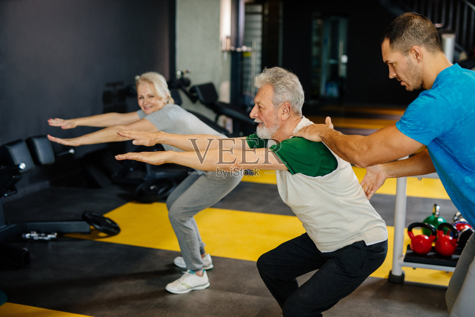 老夫妇在健身房和私人教练一起锻炼照片摄影图片