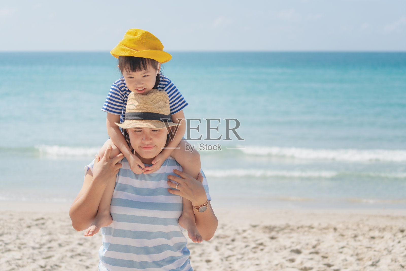 亚洲母亲和女儿在海滩上，美丽的母亲抱着女儿在他的背上在海滩上的夏天。小女孩与家人一起享受和快乐的假期，快乐的家庭理念。照片摄影图片