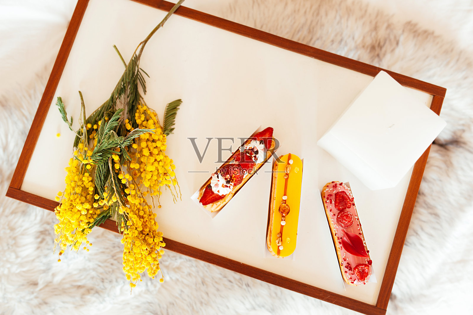 早餐托盘放在床上。用新鲜的浆果、不健康的食物和黄色的含苞欲放的花束装饰的漂亮的泡芙。照片摄影图片