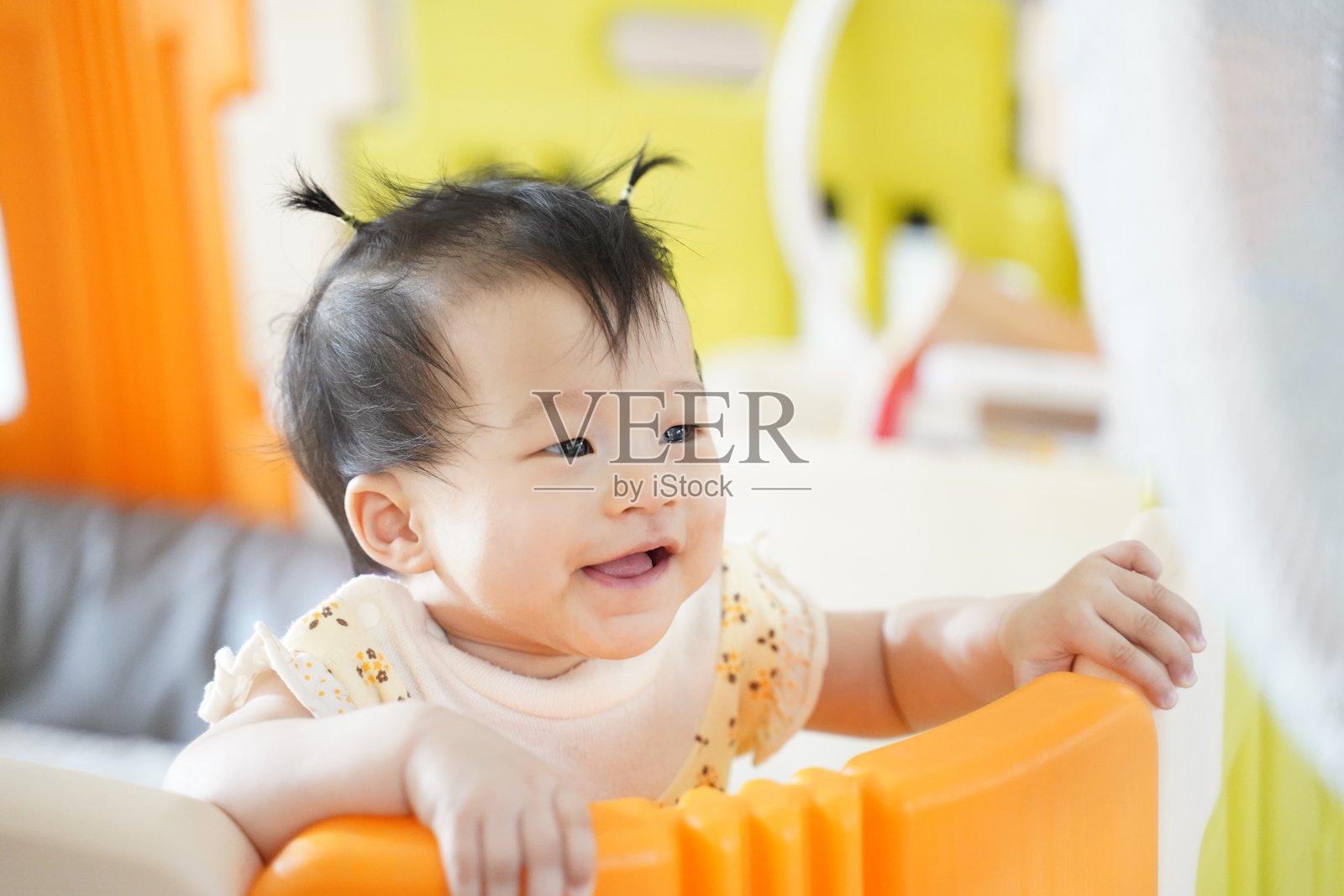 特写一个可爱的女孩8个月的婴儿微笑，爬上儿童隔断背景旁边的风扇在家里。照片摄影图片