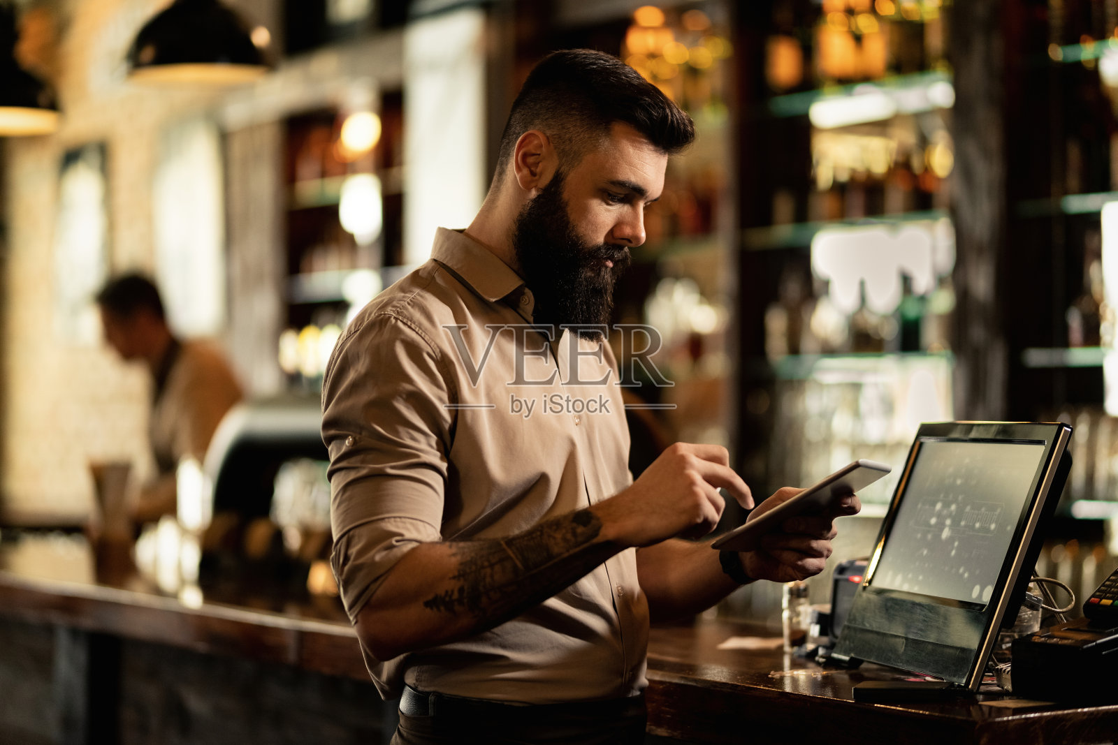 年轻的咖啡师站在酒吧收银机前使用触控板。照片摄影图片