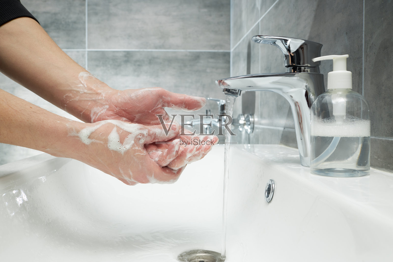 一名男子在水龙头下用抗菌肥皂洗手。在冠状病毒大流行期间用消毒剂处理双手照片摄影图片
