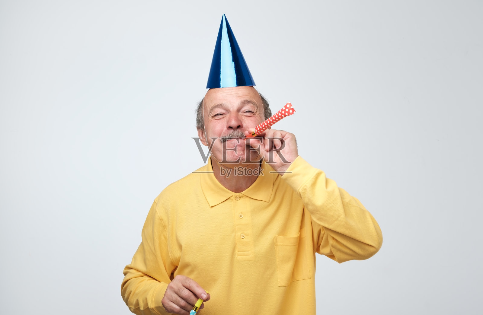 老人戴着派对帽，吹着喇叭照片摄影图片