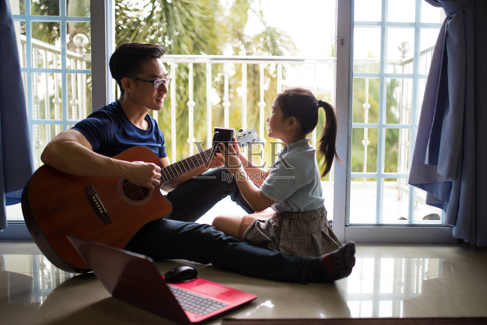 一位亚洲华人商人在家工作。在咖啡休息时间弹吉他。女儿坐在他身边，和他共度美好时光照片摄影图片