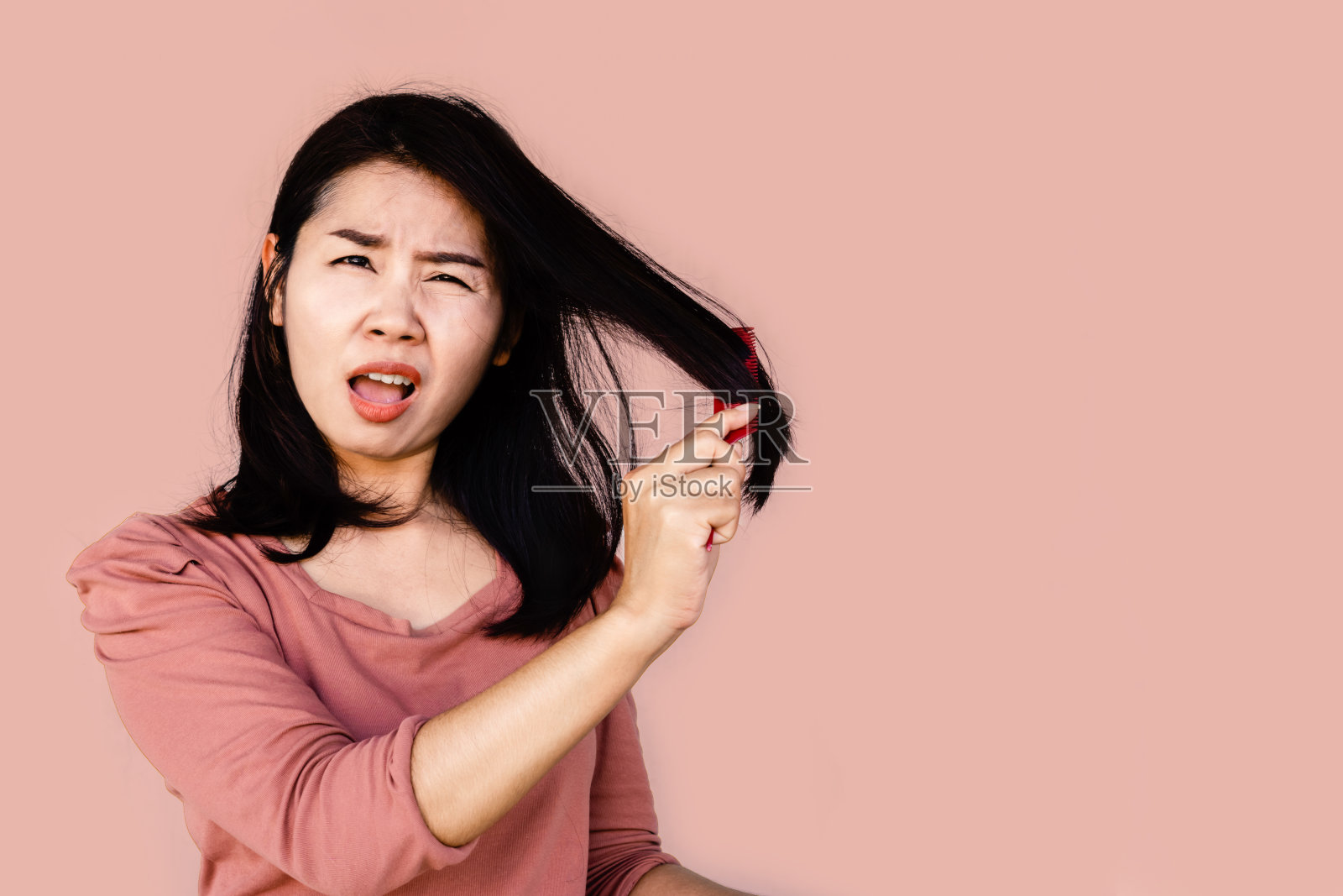 不开心的亚洲女人用化妆刷梳理她干燥受损的长发照片摄影图片
