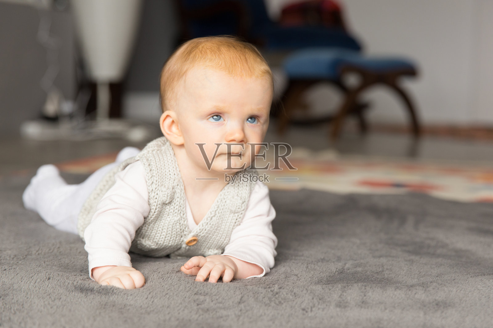 漂亮的红发女婴在灰色的地毯上爬行照片摄影图片