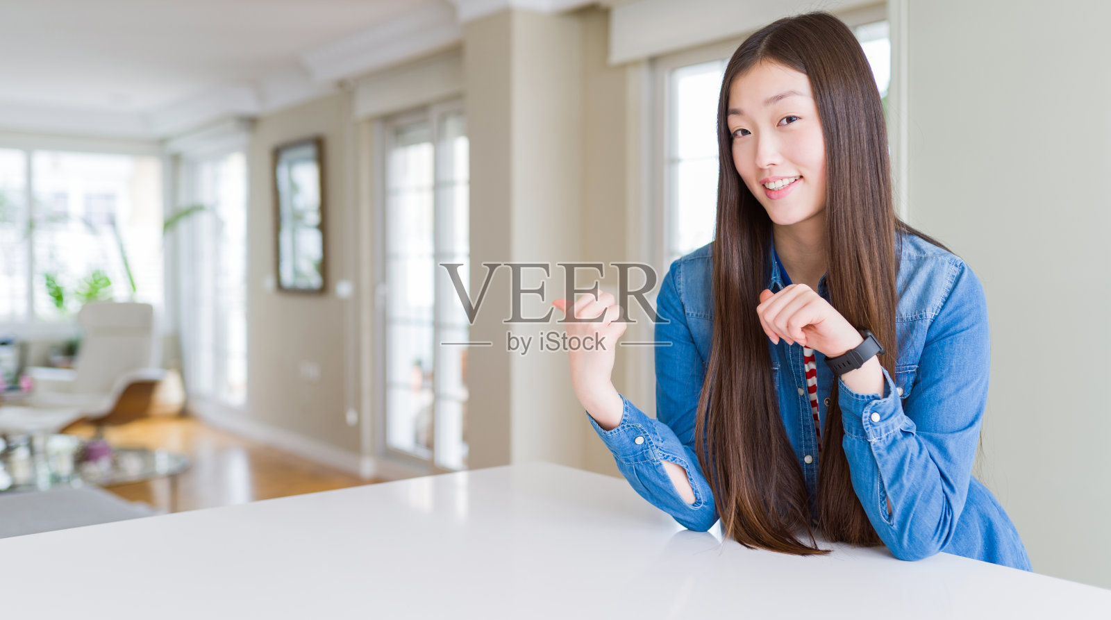 年轻美丽的亚洲女人与长头发穿着牛仔夹克指向背后与手和拇指向上，微笑自信照片摄影图片