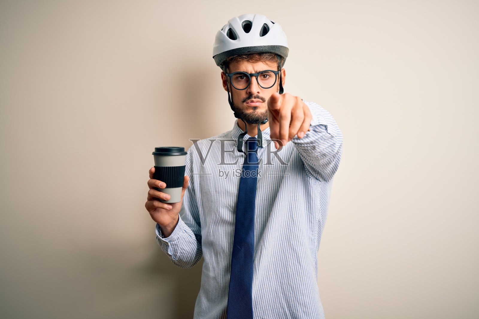 年轻的商人戴着眼镜和自行车头盔喝着咖啡，手指指着相机和你，手势，正面自信的手势照片摄影图片