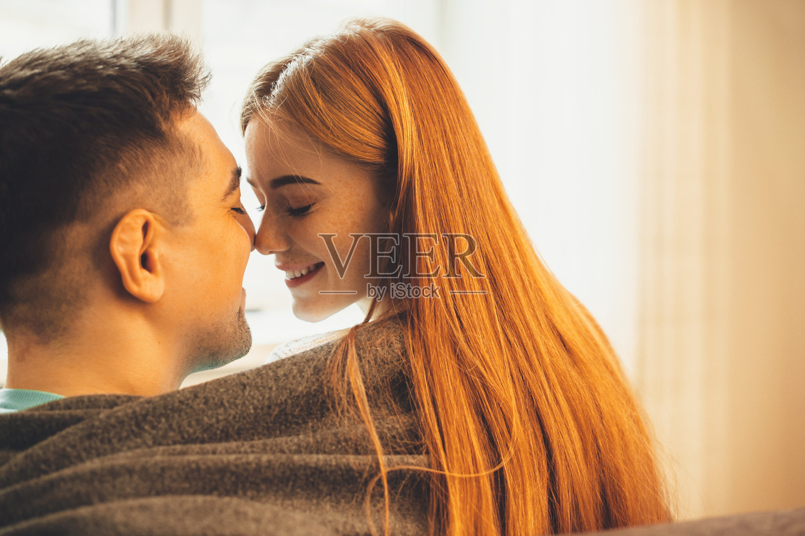 幸福的白种人夫妇盖着被子，在阳光下互相亲吻照片摄影图片