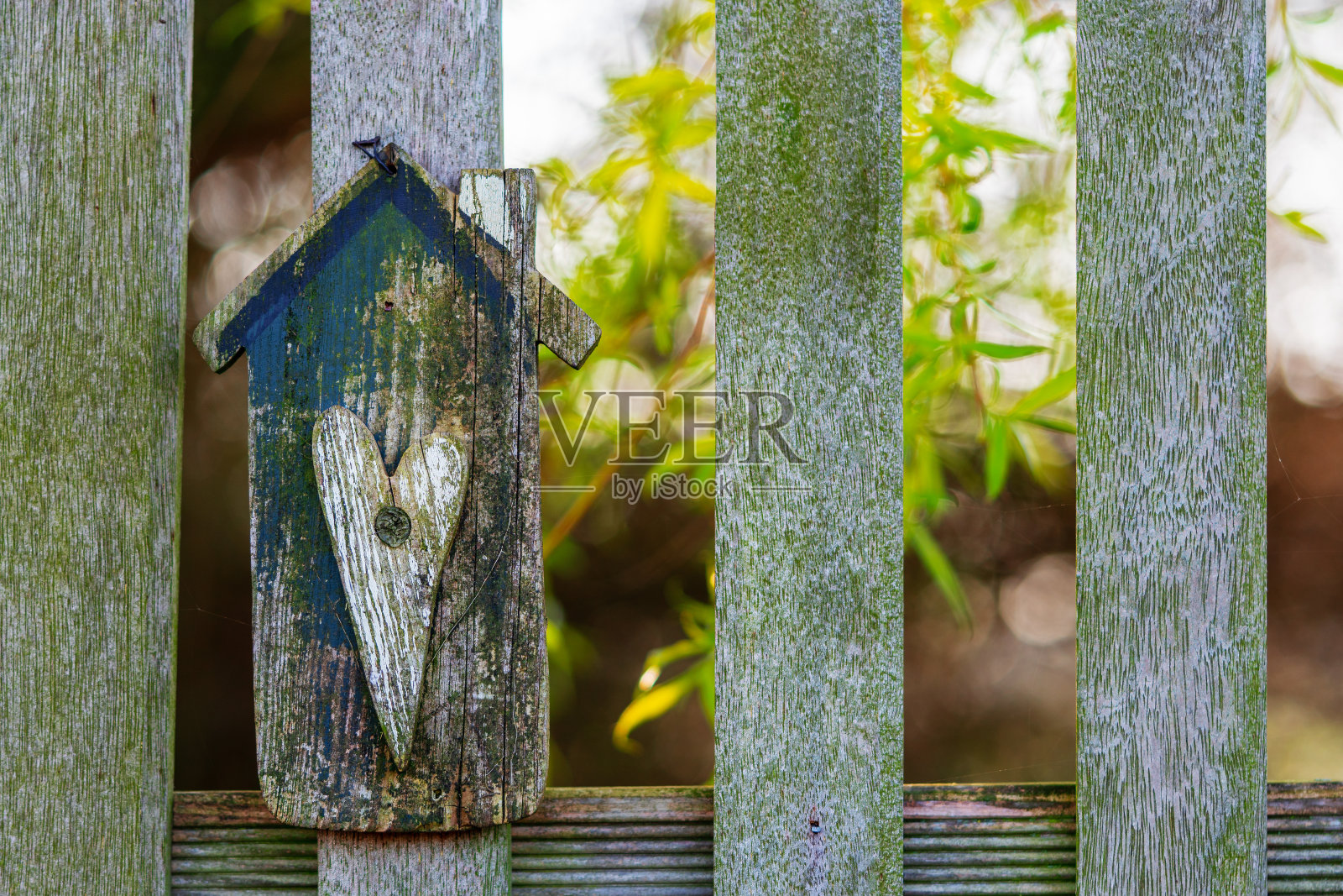 手工制作，房子形状的木面板与心形的花园篱笆。树与明亮的绿色树叶在阳光的背景。家居、园艺、家居装饰、手工或装饰的概念。照片摄影图片