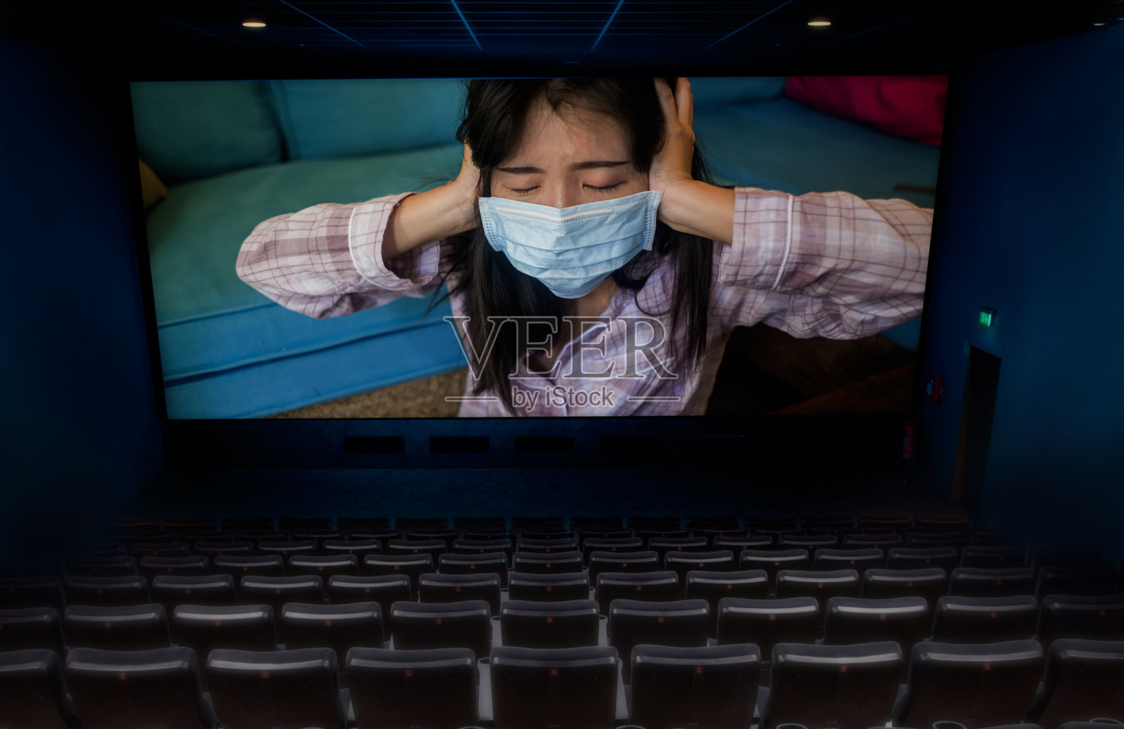 空空如也的电影院放映关于2020年COVID-19疫情的电影，屏幕上显示一名戴着防护口罩的亚洲华人妇女在被隔离的家中照片摄影图片