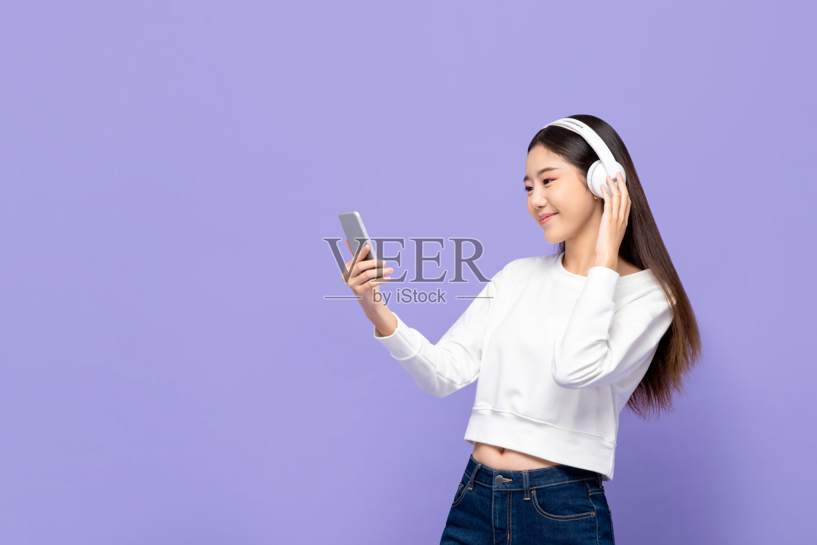 年轻微笑的亚洲妇女的肖像听音乐手机使用无线耳机在紫色孤立的工作室背景照片摄影图片