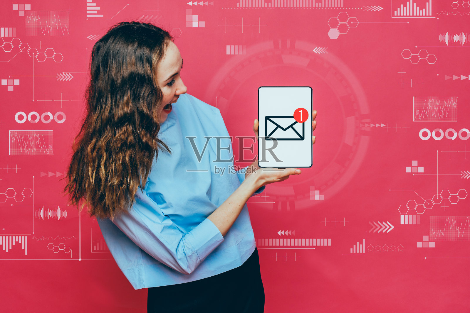 时髦的白人女孩在淡蓝色t恤在粉红色的背景。手持平板电脑与信封图标与新的信息符号。电子邮件的概念。照片摄影图片
