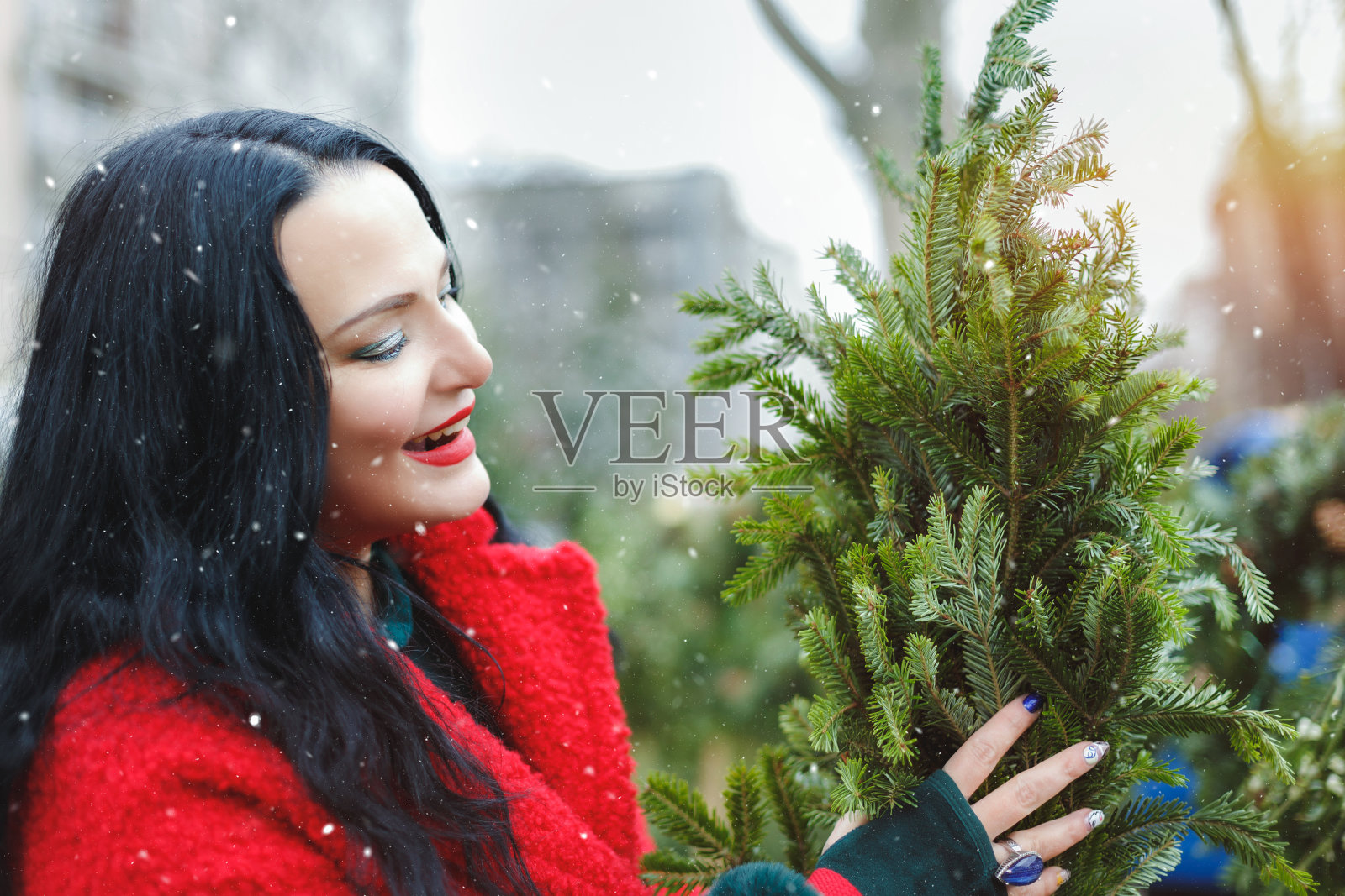 在圣诞树农场，穿着红色外套的时髦女人正在挑选常青树照片摄影图片