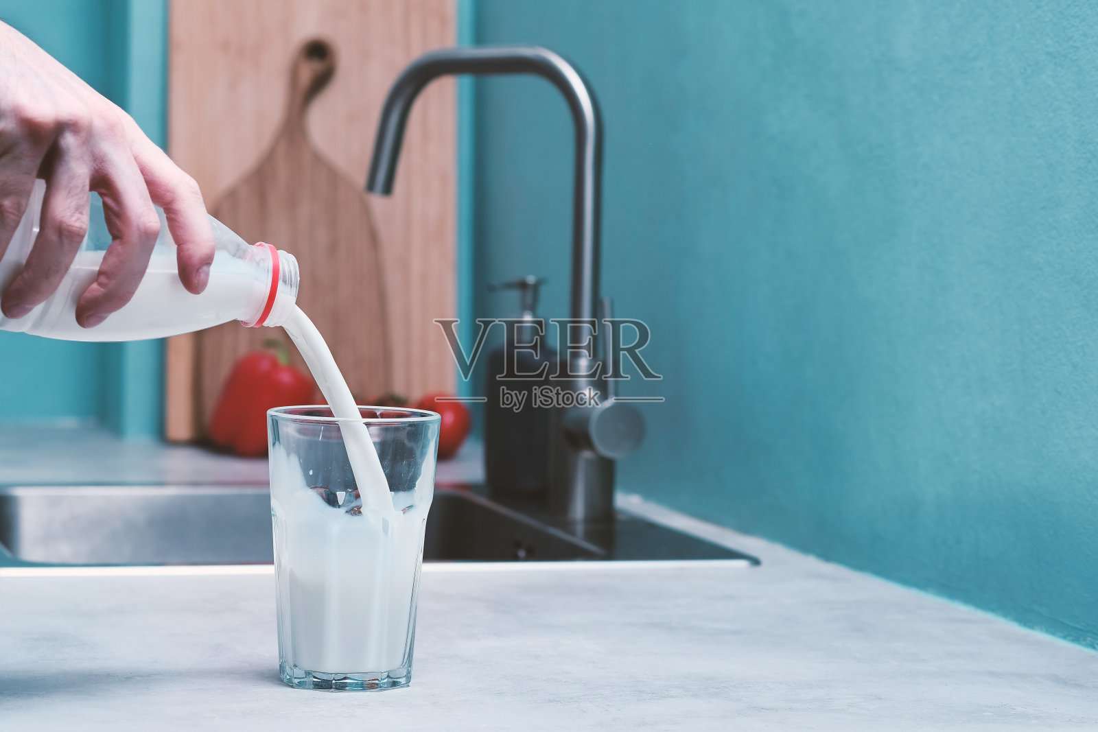 在水槽和蓝色背景的衬托下，一个男人用手将牛奶倒进厨房的玻璃杯里。为右边的文本留出空白照片摄影图片