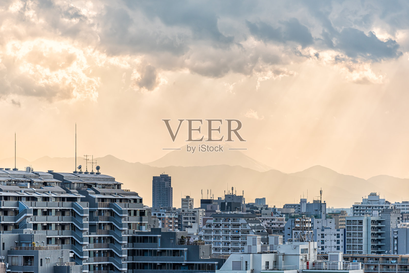 日落在东京，日本新宿城市景观剪影富士山和金色的阳光，公寓楼和山与雨云照片摄影图片