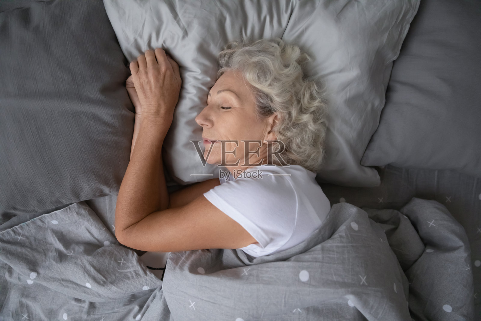 快乐成熟的女人睡在柔软的枕头下的毯子。照片摄影图片