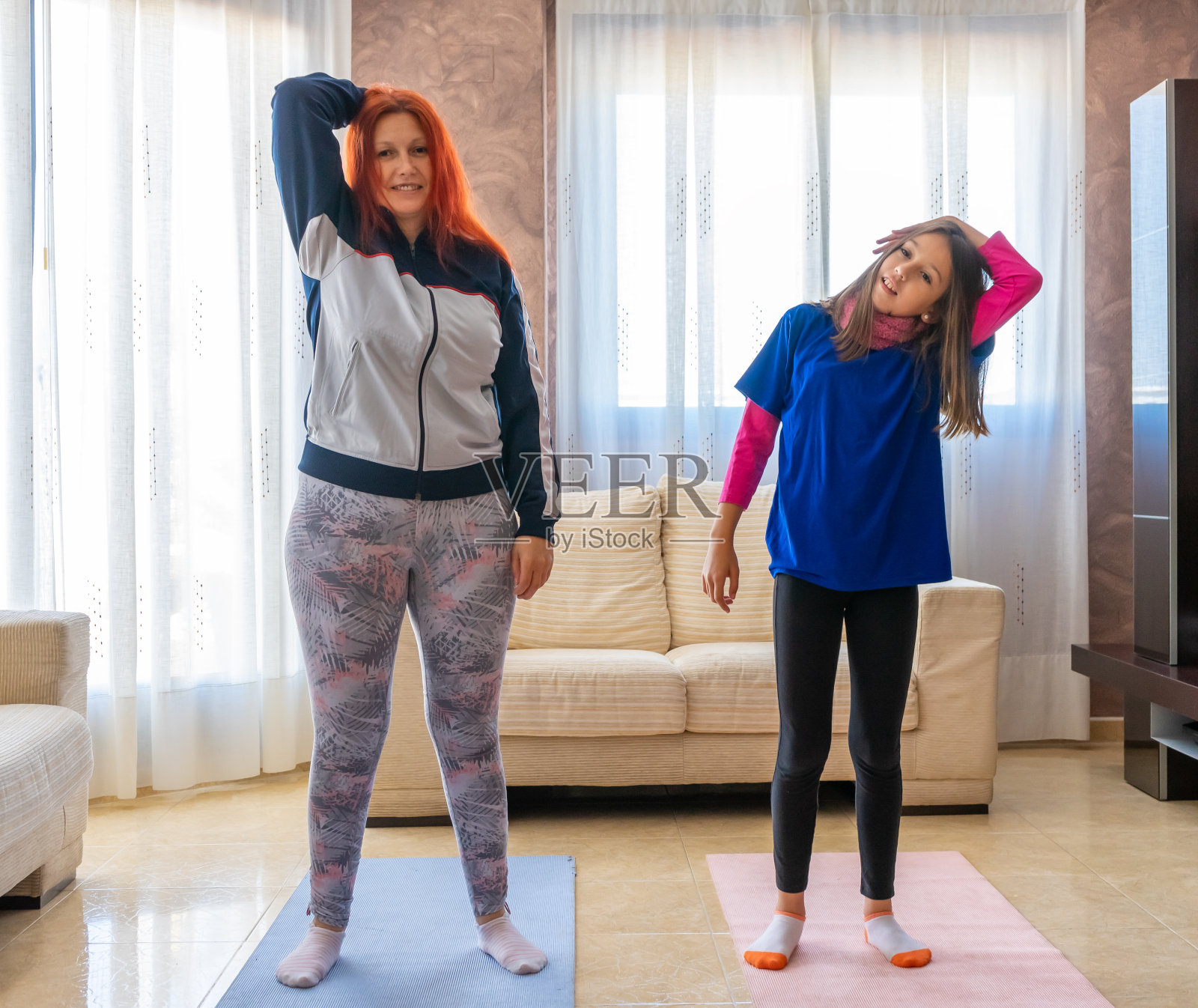 母亲和女儿穿着运动服在家里客厅的白色沙发间锻炼照片摄影图片