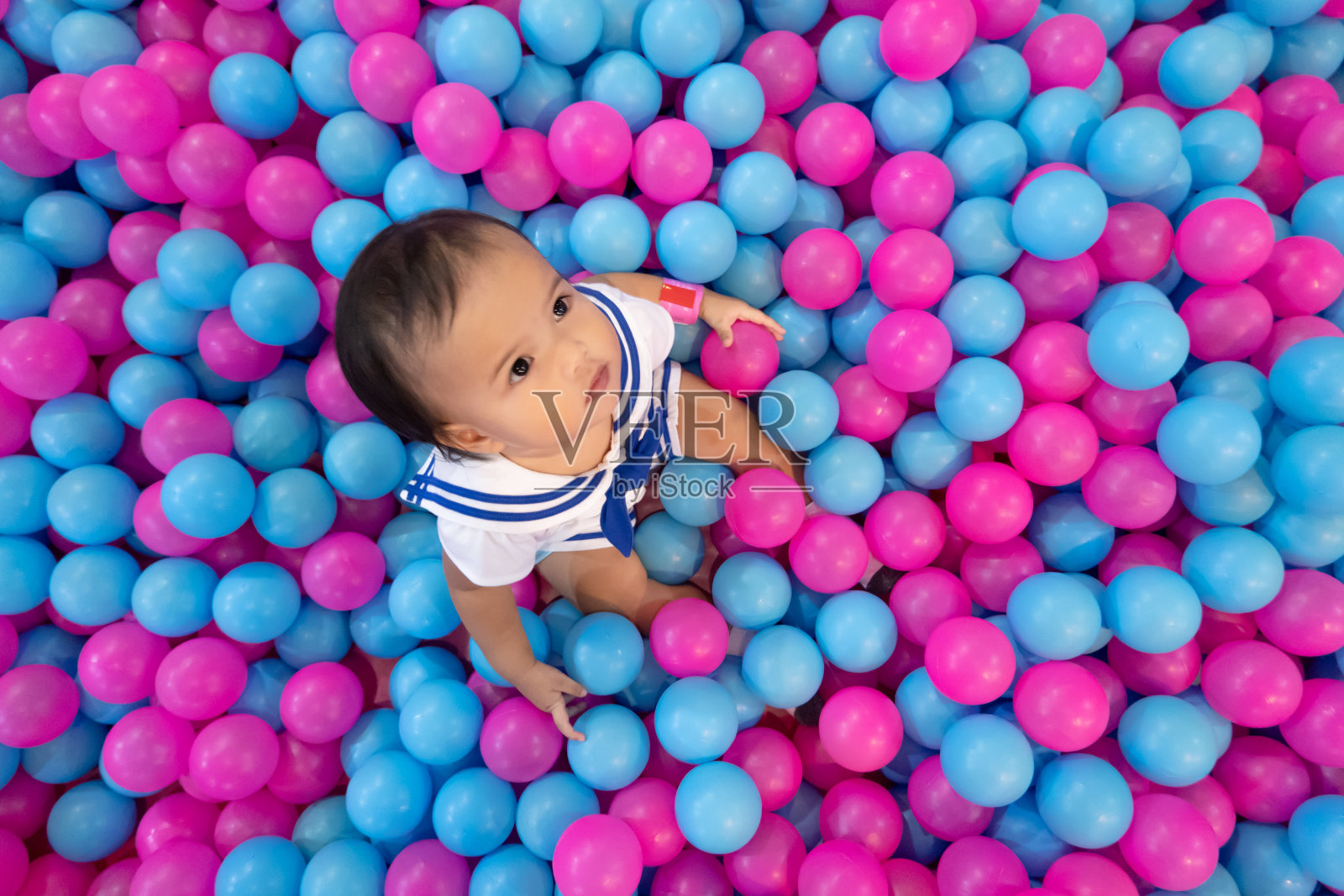 快乐的亚洲小女孩在一个装满塑料球的大干池塘里玩，孩子在室内游乐场照片摄影图片