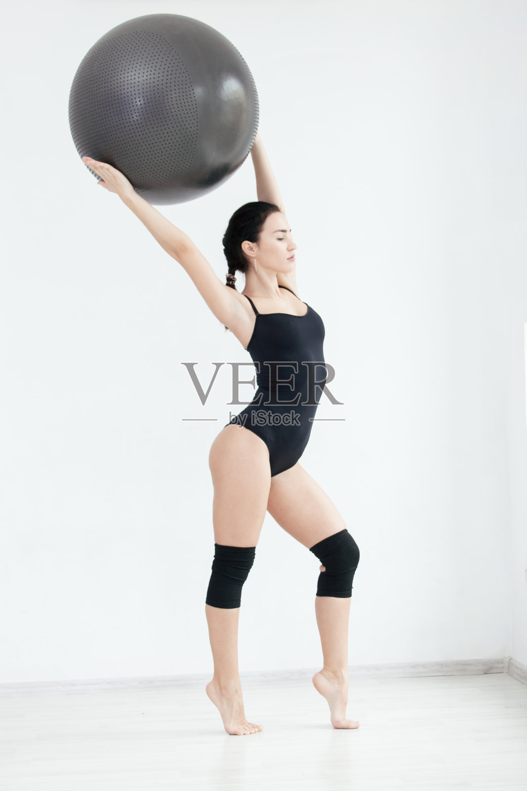 身材健美的美丽女孩在工作室摆姿势与健身球在她的头上照片摄影图片