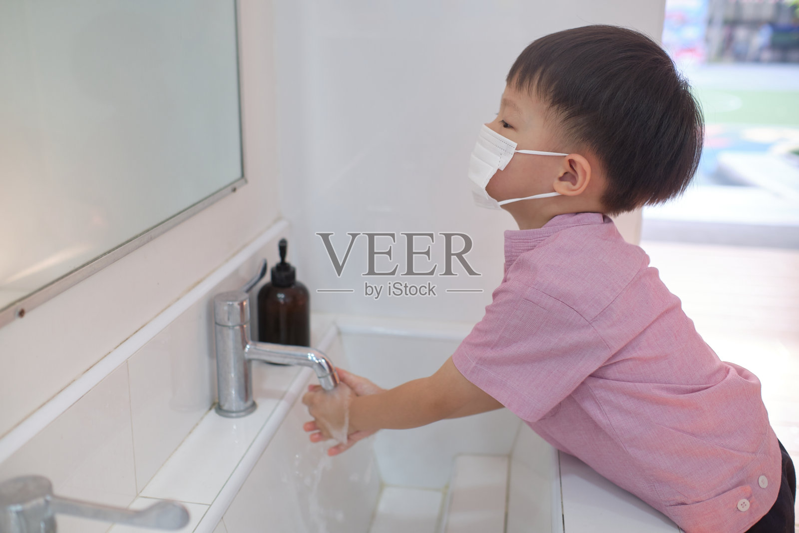 亚洲3 - 4岁小孩戴医用口罩在公共厕所洗手池上自己洗手，卫生概念-柔软和选择性的焦点照片摄影图片