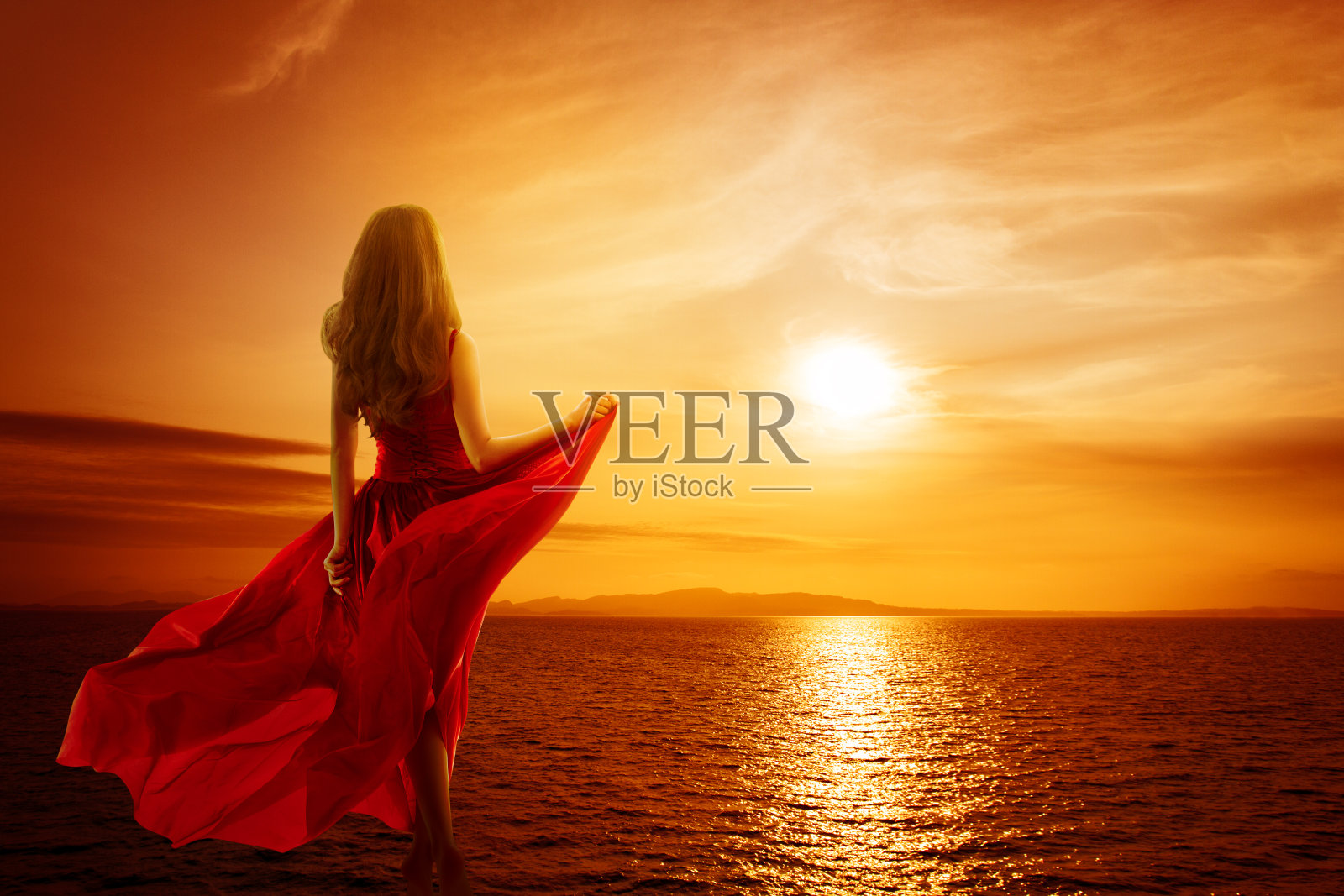 女人在海边看日落的天空，女孩在风中飘扬的红衣服，后视图照片摄影图片