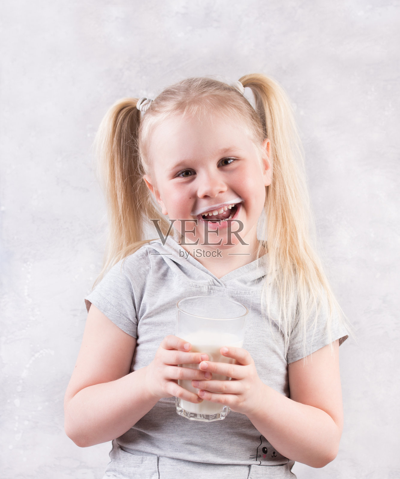 一个小女孩拿着一杯牛奶的肖像，映衬着灰色的背景。照片摄影图片