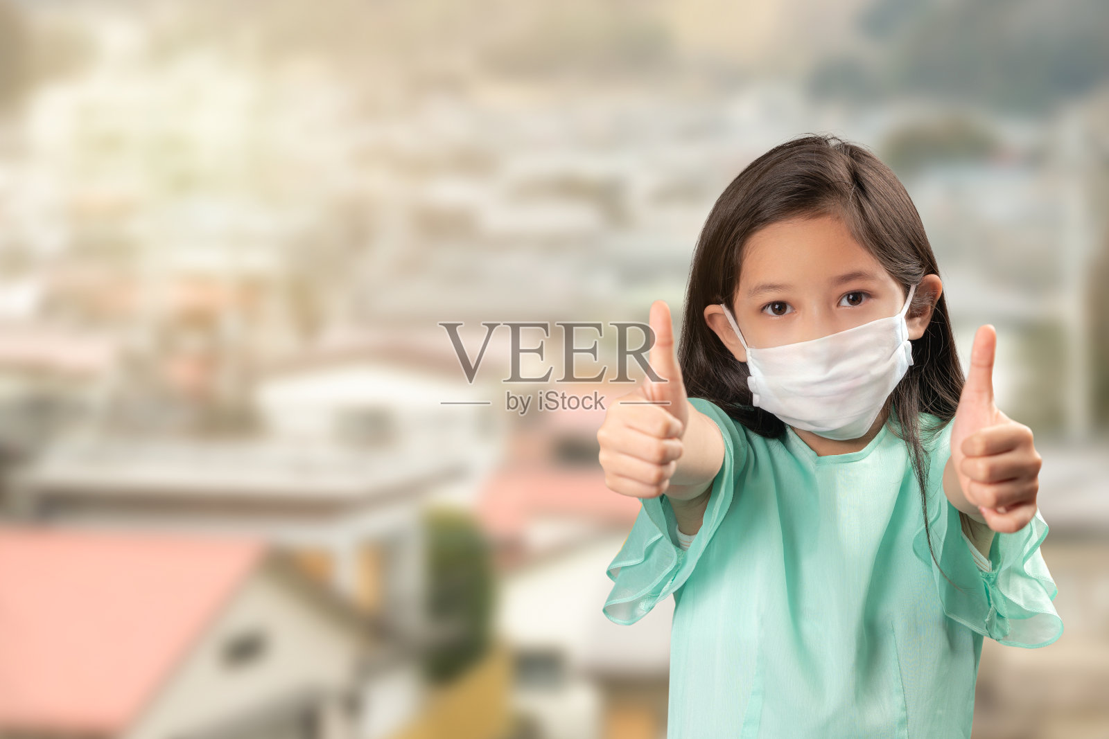 亚洲可爱女孩戴着口罩保护新冠病毒或COVID-19。戴着白色面罩的孩子竖起大拇指或有好迹象。PM 2.5空气污染。带有复制空间的医疗保健概念。照片摄影图片