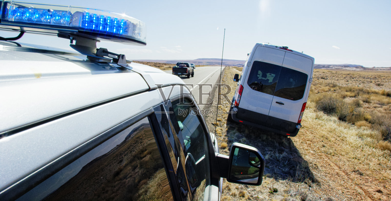 在一个阳光明媚的日子里，一辆开着灯的警车在犹他州沙漠的州际公路旁拦下了一辆大型白色面包车照片摄影图片