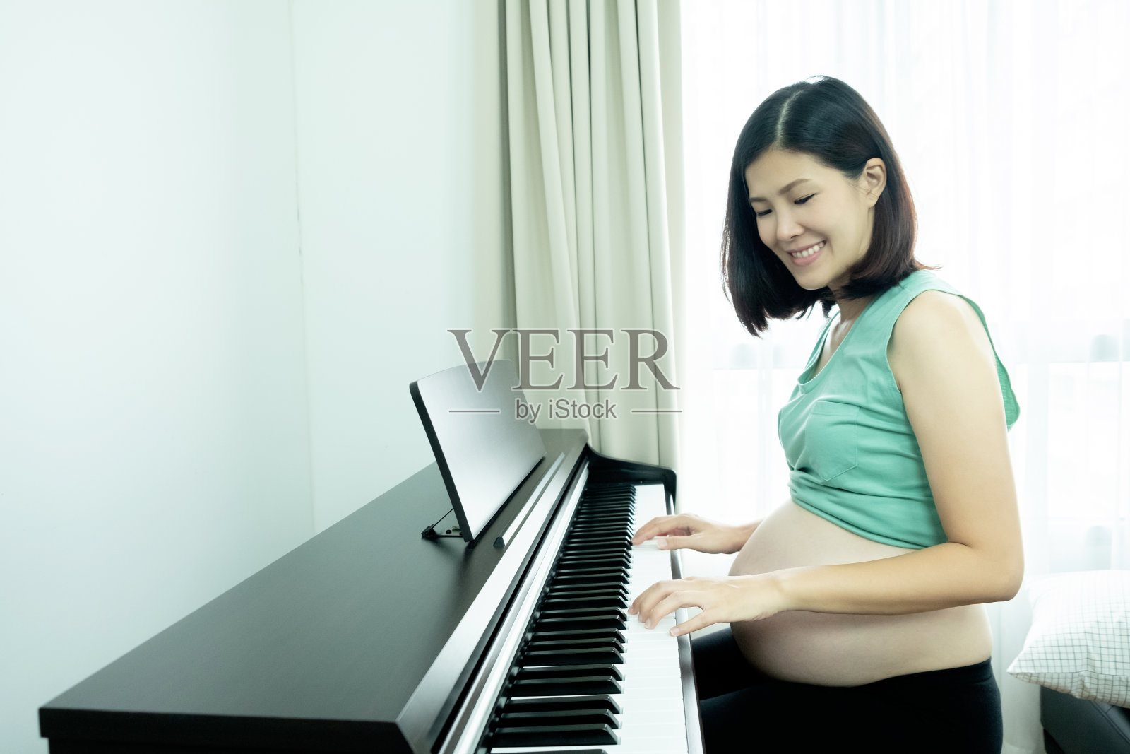 美丽的亚洲孕妇弹钢琴与她的双手为她的孩子。快乐的母亲的概念。照片摄影图片