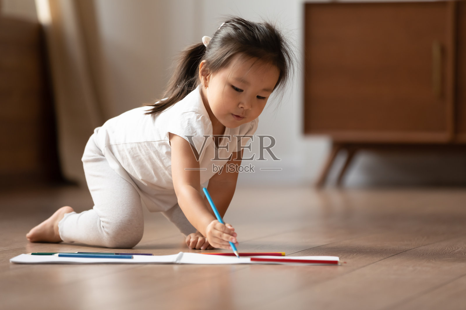 在温暖的地板上，一个亚洲小女孩在画册上画画照片摄影图片