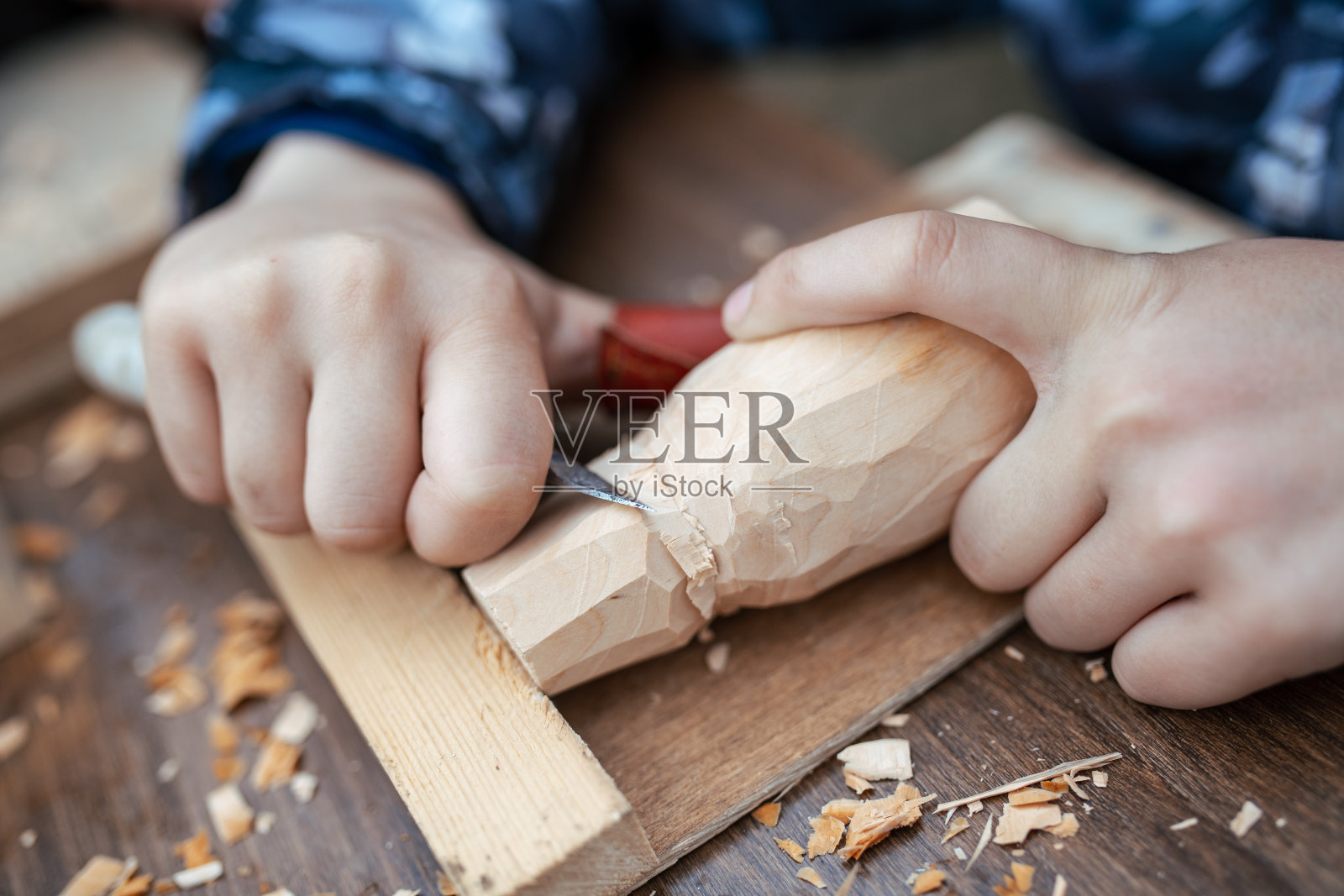 孩子用小刀在木头上雕刻玩具。木匠在车间里。手的特写照片摄影图片