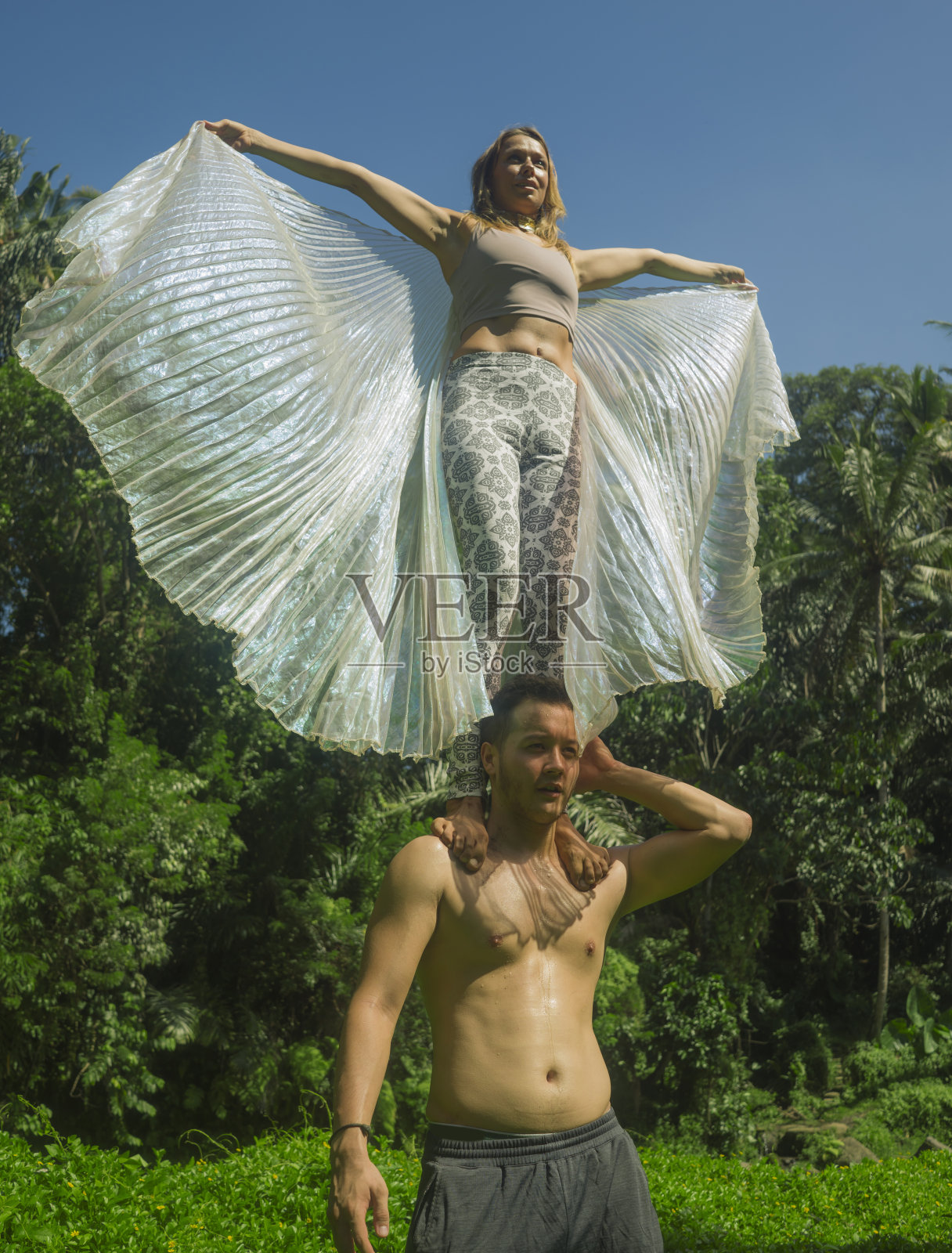 年轻迷人的情侣在热带的绿色森林里做acroyoga，享受大自然，女孩展开翅膀，站在男人的肩膀上保持平衡，健康的生活方式和健身照片摄影图片