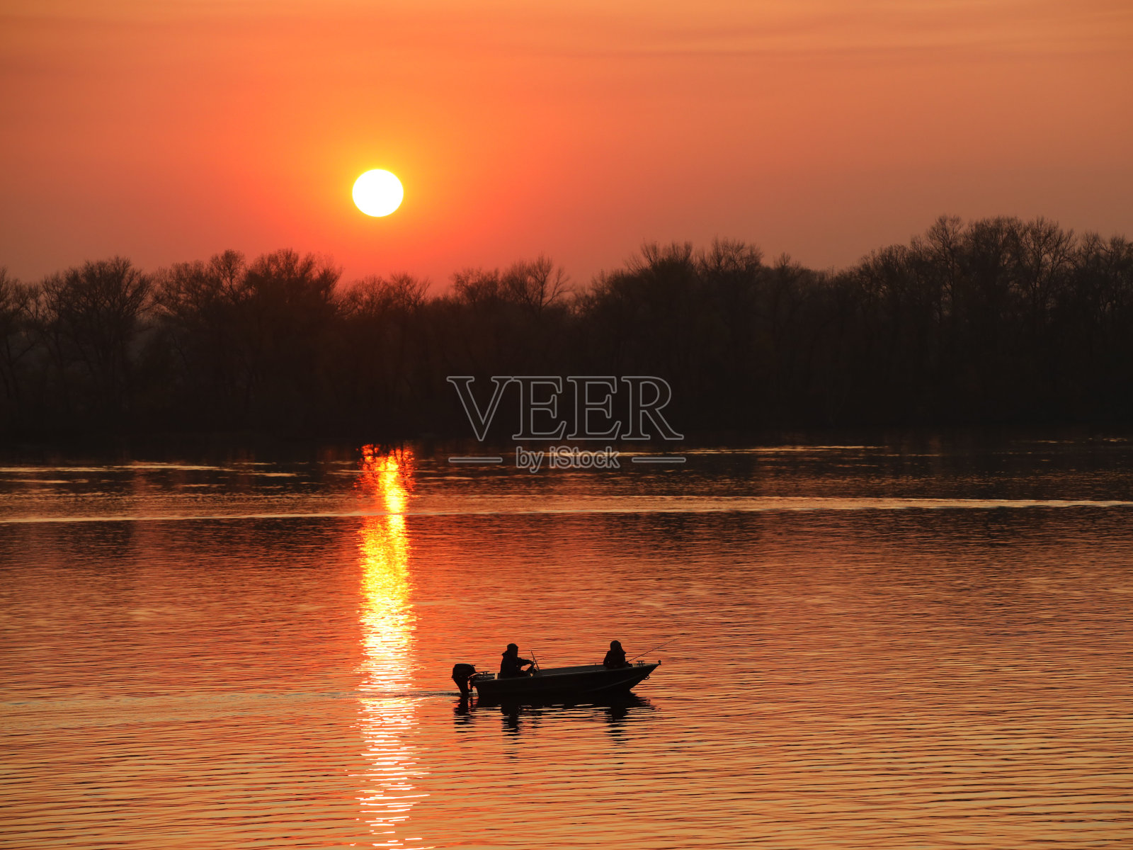 两名渔民，一男一女，在橙色的夕阳背景下，在河上的摩托艇上游泳。浪漫的氛围。晚上钓鱼。旅游被水。一种自然现象照片摄影图片