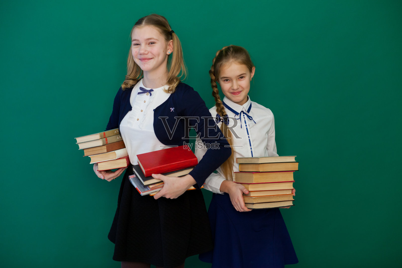 两个女学生拿着书站在教室的绿板前学习照片摄影图片
