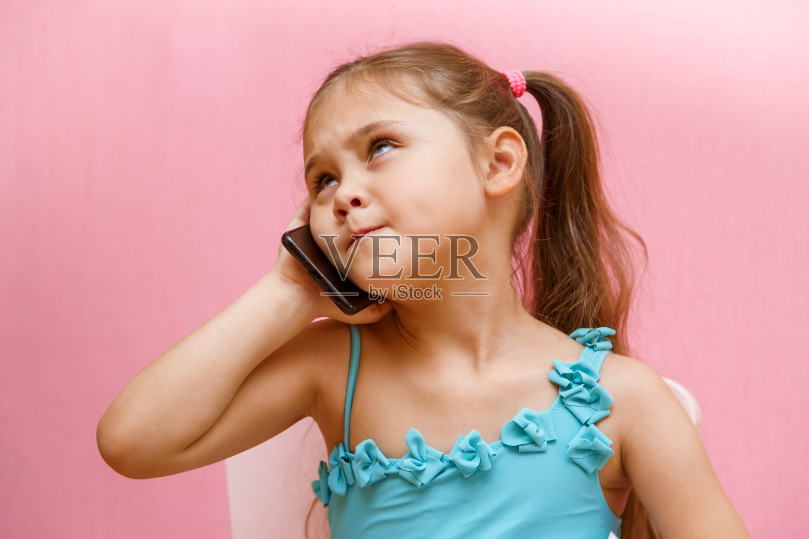 粉色背景下的小女孩正在打电话照片摄影图片