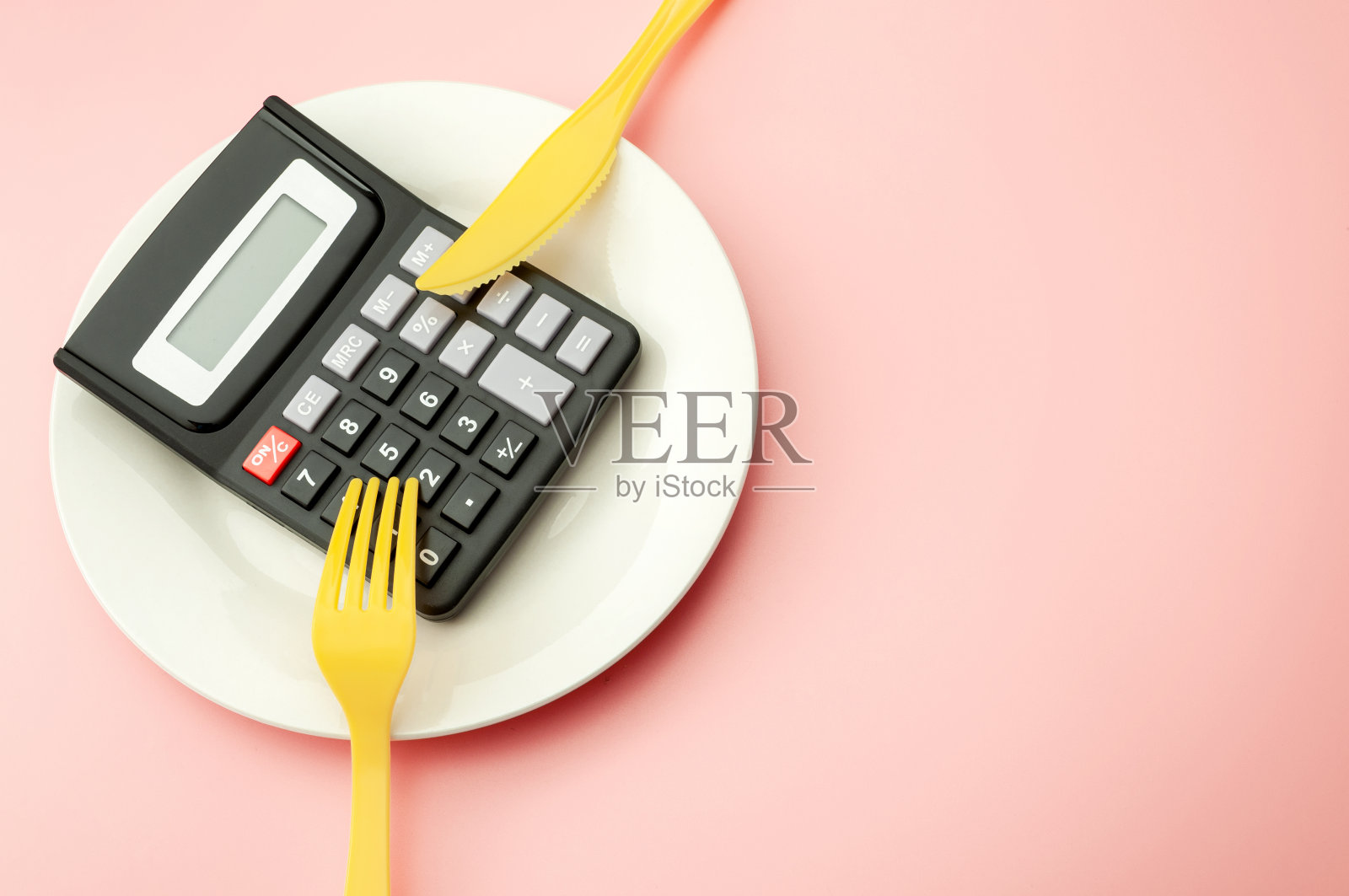 计算昂贵的食物支出成本，计算卡路里和减肥计划的概念与空盘子上的计算器，黄色的叉和刀孤立在粉红色的背景与复制空间照片摄影图片