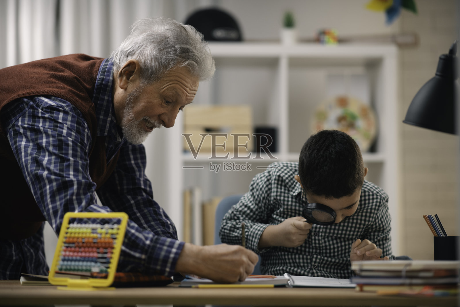 爷爷和孙子一起做作业。照片摄影图片
