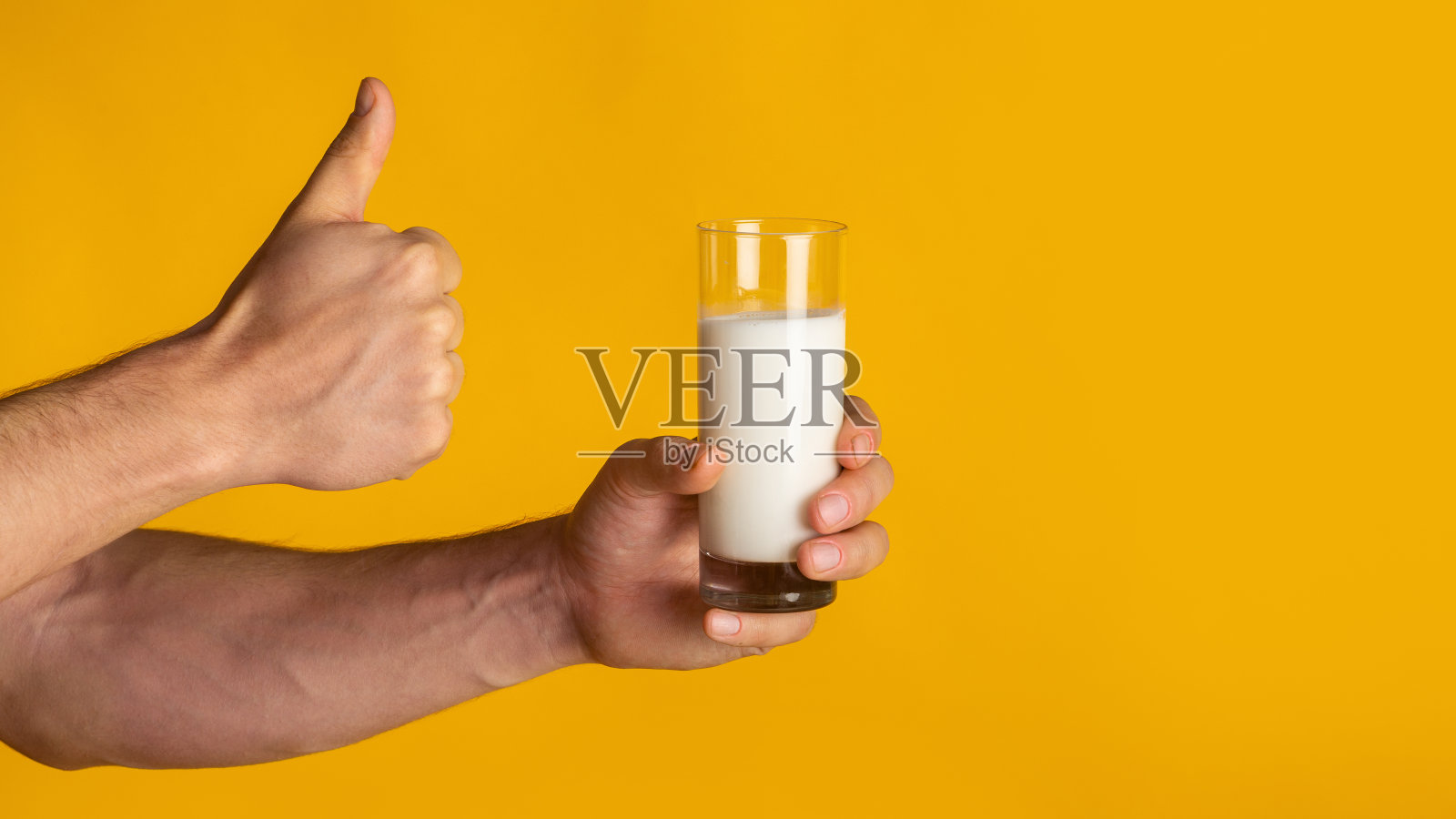不认识的人与一杯新鲜牛奶显示大拇指向上的手势在橙色的背景，特写。本空间照片摄影图片