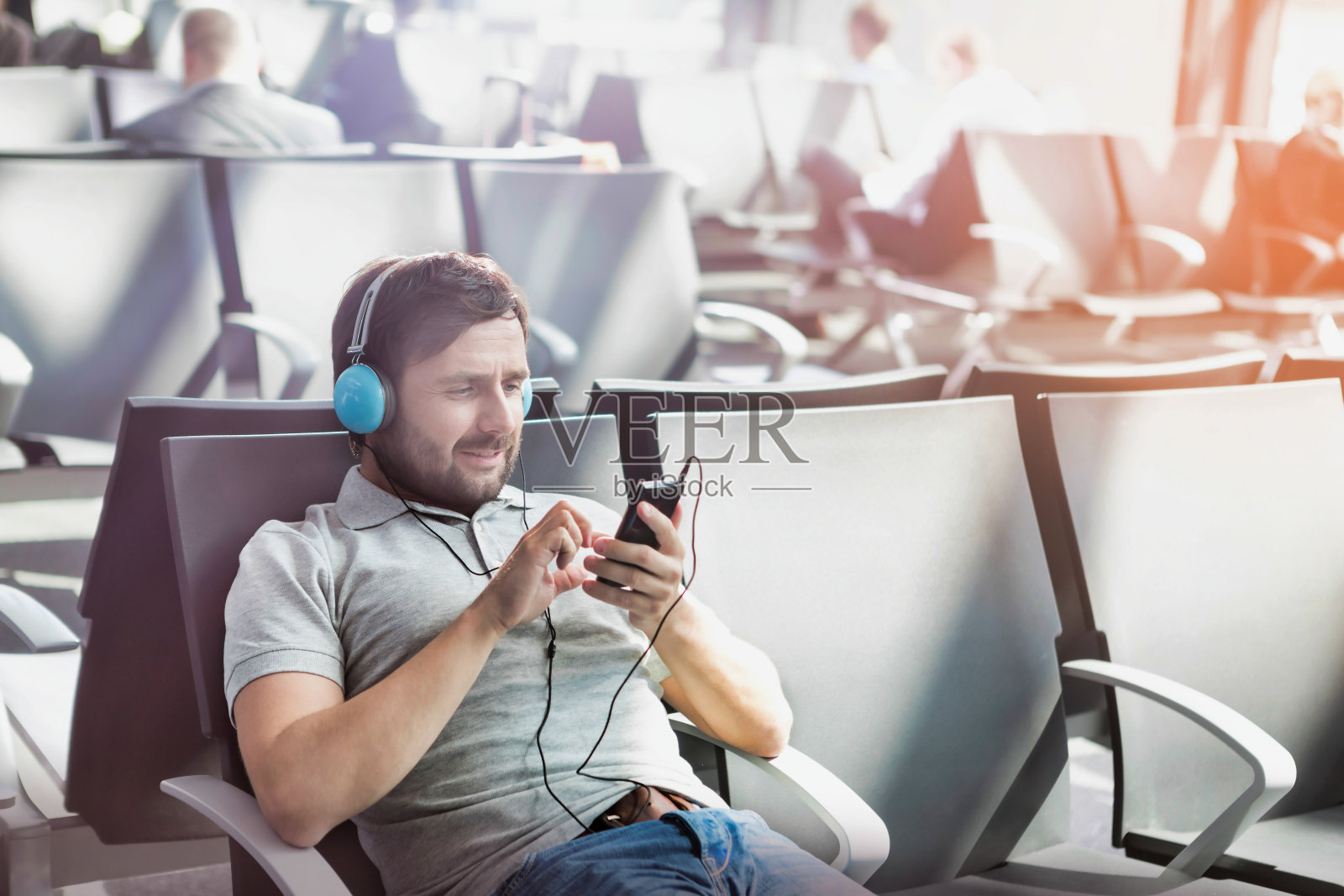 一名男子在机场等待登机时戴着耳机使用智能手机的肖像照片摄影图片